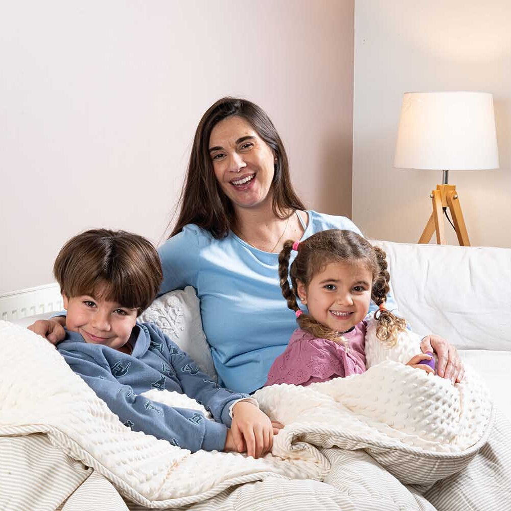 Mamá con dos niños sentados en la cama, compartiendo el Plumón Minky Líneas Café ally's en tono crema.