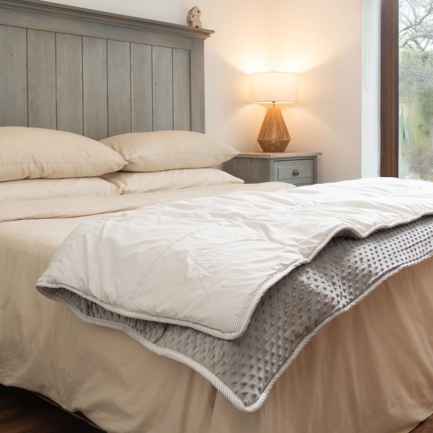 Plumón Minky Líneas Grises ally's tendido sobre la cama, doblado en una esquina para mostrar sus dos caras: minky gris con relieve de puntos por dentro y algodón de rayas grises por fuera.