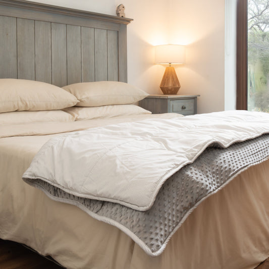 Plumón Minky Líneas Grises ally's tendido sobre la cama, doblado en una esquina para mostrar sus dos caras: minky gris con relieve de puntos por dentro y algodón de rayas grises por fuera.